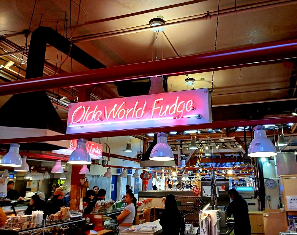 The neon Olde World Fudge sign hanging over the counter in Granville Island Public Market
